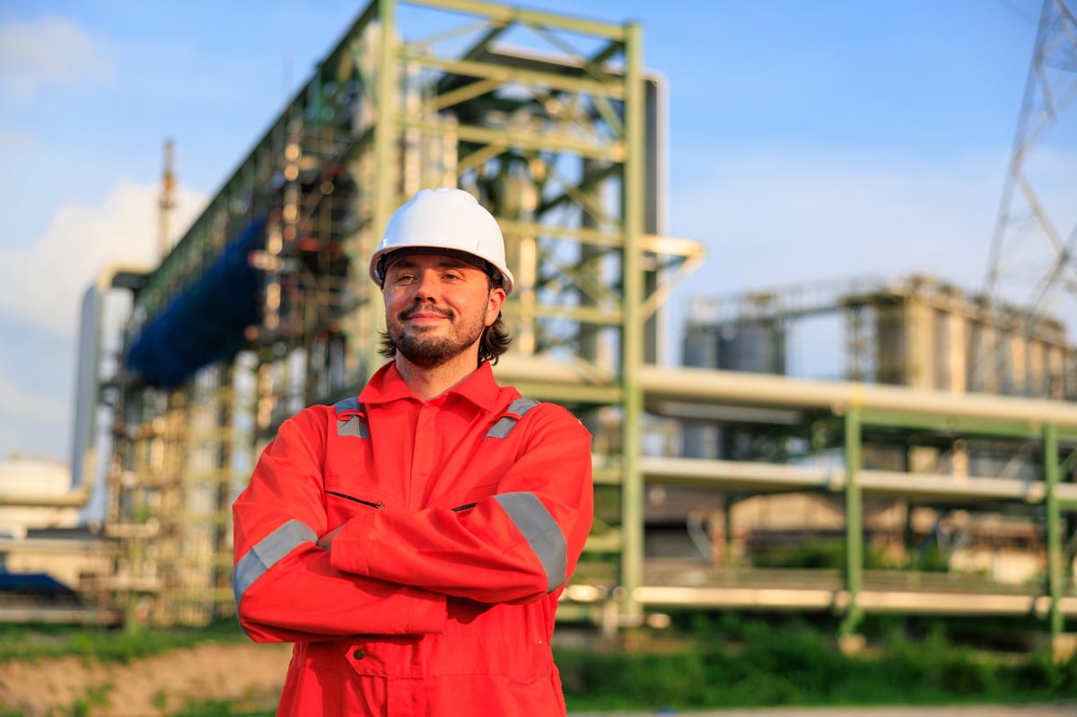 Ghanaian worker in orange coveralls and hard hat at a refinery at sunset