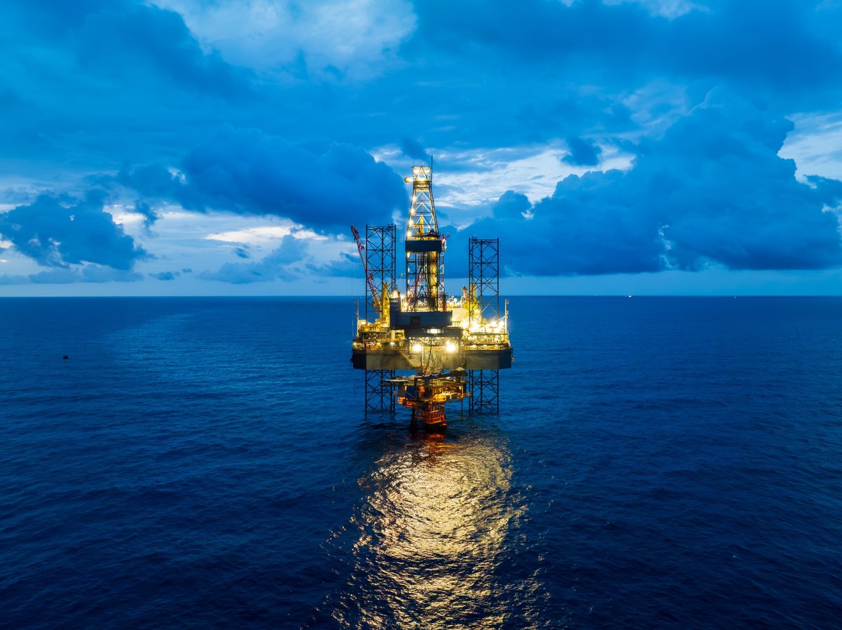 Offshore drilling platform lit up at dusk, seen from the water